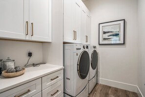 A laundry area with a washing machine and dryer, a countertop with jars, and a framed picture on the wall. - Pecan Valley 5205/5193|2 Private Pools&Spas, Private Pickleball Court, Game Room (Hurricane)