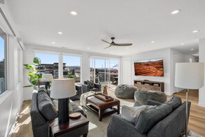 A spacious living room with a modern design, featuring a large flat-screen TV, comfortable seating, and a view of the cityscape through large windows. - Pecan Valley 5205/5193|2 Private Pools&Spas, Private Pickleball Court, Game Room (Hurricane)