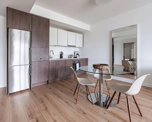 Une cuisine moderne avec des meubles en bois, des appareils en acier inoxydable et une table à manger en verre, assortie de chaises blanches.