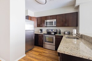 A modern kitchen with dark wooden cabinets, stainless steel appliances, and a granite countertop. - Gorgeous One Bedroom - 5-min Walk from Metro-North (White Plains)