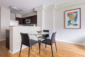 A modern kitchen with dark cabinets, a white countertop, and a glass dining table with black chairs. - Gorgeous One Bedroom - 5-min Walk from Metro-North (White Plains)