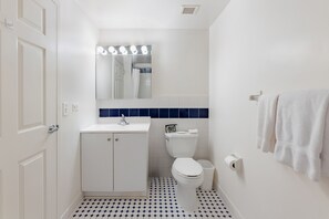 Um banheiro com pia branca, espelho iluminado, vaso sanitário e piso revestido em azul.
