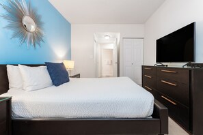 Quarto com cama, penteadeira, televisão e espelho.