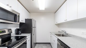 Una cocina moderna con armarios blancos, un refrigerador de acero inoxidable, una estufa negra y un lavavajillas.