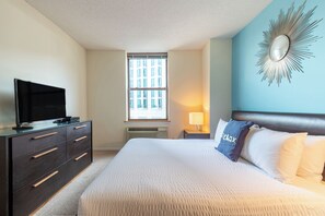 A hotel room with a bed, a dresser, a television, a window, and a wall-mounted mirror.