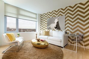 A modern living room with a white sofa, a round gold coffee table, and a large window with a view of the city.