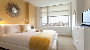Une chambre d’hôtel avec un lit, une grande fenêtre avec des stores, une télévision et un grand miroir décoratif au mur.