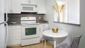 Une cuisine moderne avec des meubles blancs, un four à micro-ondes, une cuisinière, un four et une petite table à manger agrémentée d’un saladier.