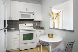 A modern kitchen with white cabinets, a microwave, stove, oven, and a small dining table with a bowl.