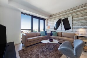 Een moderne woonkamer met een bank, salontafel, fauteuil en een groot raam met uitzicht op de stad.