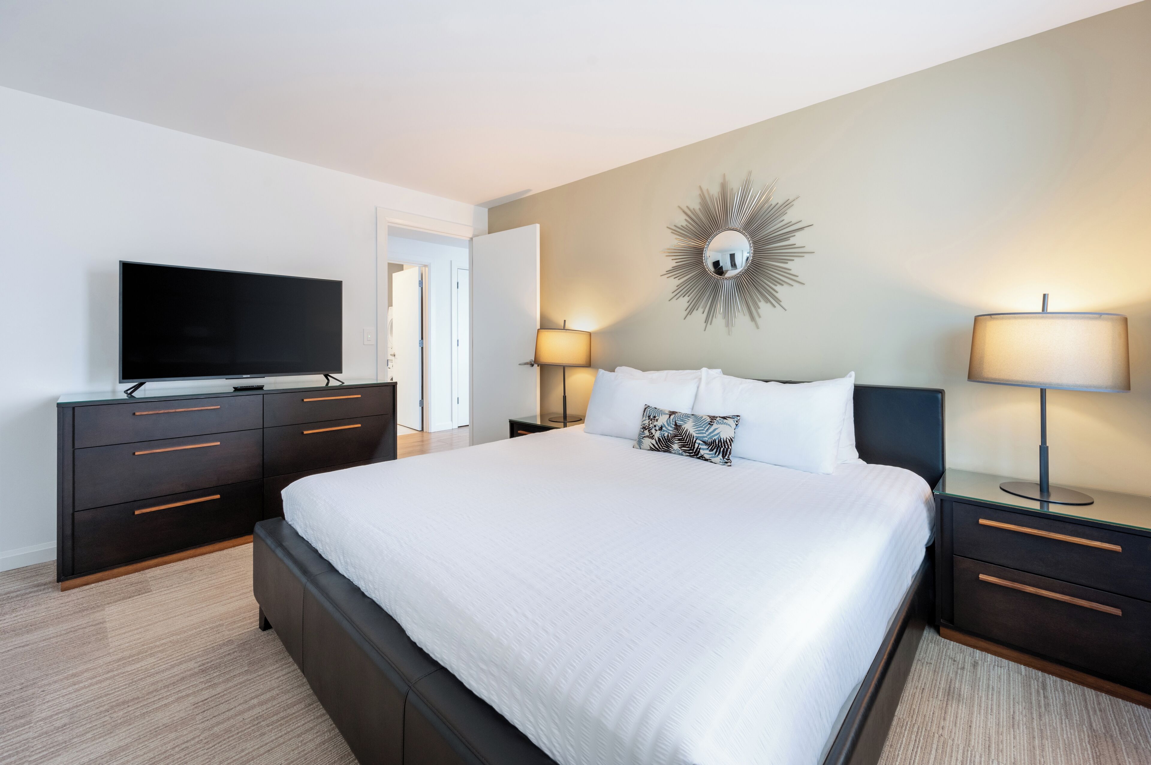 Une chambre d’hôtel moderne dotée d’un grand lit, d’un téléviseur à écran plat, de deux lampes de chevet et d’un grand miroir décoratif au mur.
