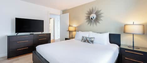 Une chambre d’hôtel moderne dotée d’un grand lit, d’un téléviseur à écran plat, de deux lampes de chevet et d’un grand miroir décoratif au mur.