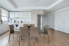 Eine moderne Küche mit weißen Schränken, einem Edelstahlkühlschrank und einem Essbereich mit einem Glastisch und Stühlen.