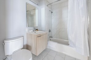 A modern bathroom with a toilet, sink, mirror, and bathtub.