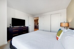 A hotel room with a large bed, a TV on a dresser, a lamp, and a door leading to a bathroom. - Serviced 1 Bedroom Across From Fenway Park (Boston)