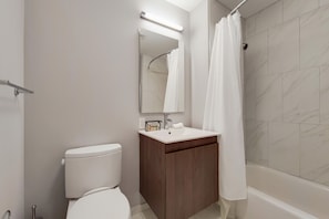 A modern bathroom with a toilet, a wooden vanity with a mirror, and a shower area.