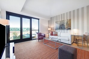 Una sala de estar moderna con un ventanal grande, un sofá blanco, un sillón rojo, una mesa de centro de vidrio y una pared a rayas.