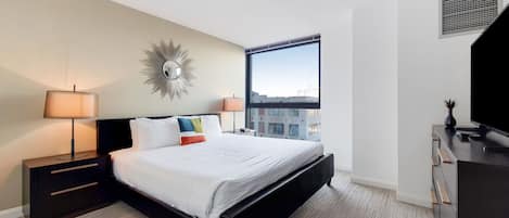 A modern hotel room with a large bed, two bedside tables with lamps, a dresser, and a large window offering a city view.