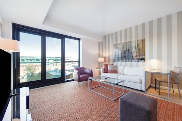 A modern living room with a large window, a white sofa, a red armchair, a glass coffee table, and a striped wall.