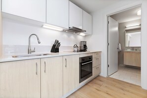 A modern kitchen with a stainless steel sink, a kettle, and a coffee maker. There are cabinets and a countertop.