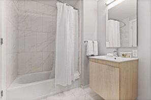A modern bathroom with a bathtub, a shower curtain, a sink with a mirror, and a wooden cabinet.