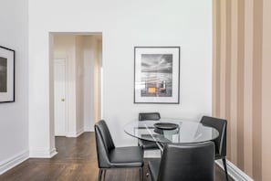 A modern dining area with a glass table and black chairs, framed artwork on the wall, and a door leading to another room.