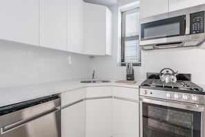 A modern kitchen with white cabinets, stainless steel appliances, a gas stove, a microwave, and a window with blinds.