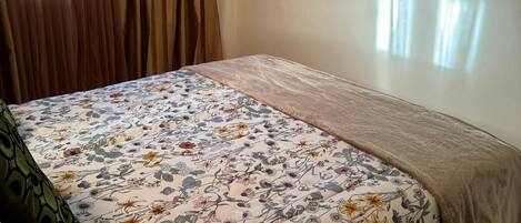 Ein Schlafzimmer mit geblümter Bettdecke, einem flachbildfernseher an der Wand und einer Klimaanlage über dem Fenster.