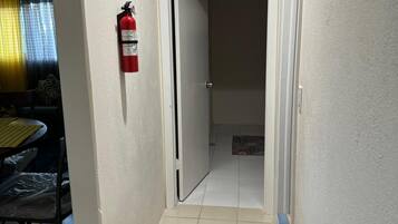 A narrow hallway with a fire extinguisher mounted on the wall, a patterned rug on the floor, and a door leading to another room.