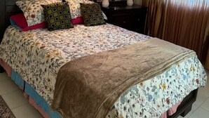 Een slaapkamer met een bed, nachtkastje, spiegel en gordijnen.