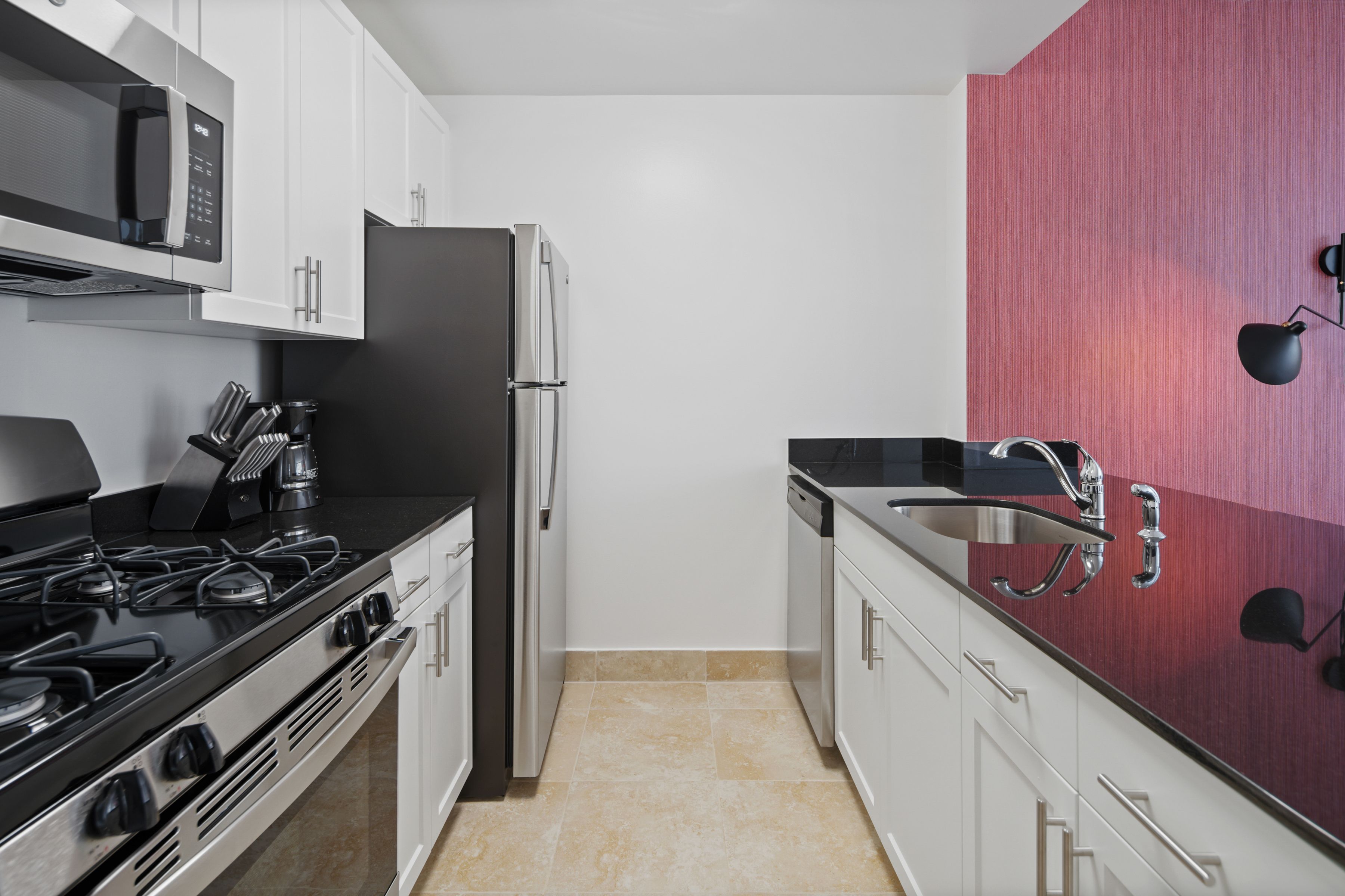 Cocina moderna con armarios blancos, un refrigerador de acero inoxidable, una estufa a gas y una encimera negra.