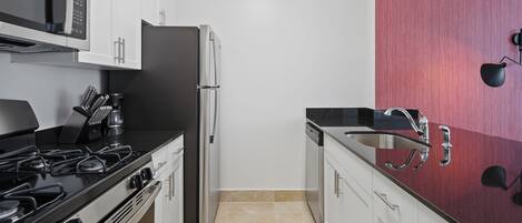 Cocina moderna con armarios blancos, un refrigerador de acero inoxidable, una estufa a gas y una encimera negra.