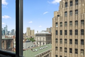 A view of a cityscape through a window, featuring a mix of modern and historic buildings, including a prominent brick building with a grid pattern and a large building with a dome.