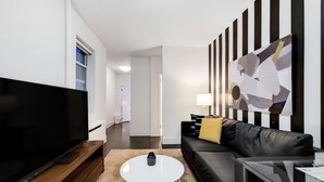 Ein modernes Wohnzimmer mit Flachbildfernseher, Couchtisch, Sofa und einem Gemälde an der Wand.