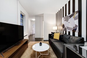Een moderne woonkamer met een flatscreen televisie, een bijzettafeltje, een bank en een schilderij aan de muur.