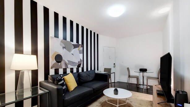 Ein modernes Wohnzimmer mit einer schwarzen Couch, einem Couchtisch, einem Fernseher und einem Gemälde an der Wand.