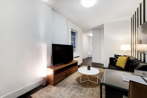 A modern living room with a flat-screen TV, a small round table, a sofa with a yellow pillow, and a 'No Smoking' sign. - Elevated Chelsea Living | Pet-Friendly (New York)