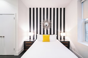 A hotel room with a large bed, two bedside tables with lamps, a black and white striped wall, and a window.