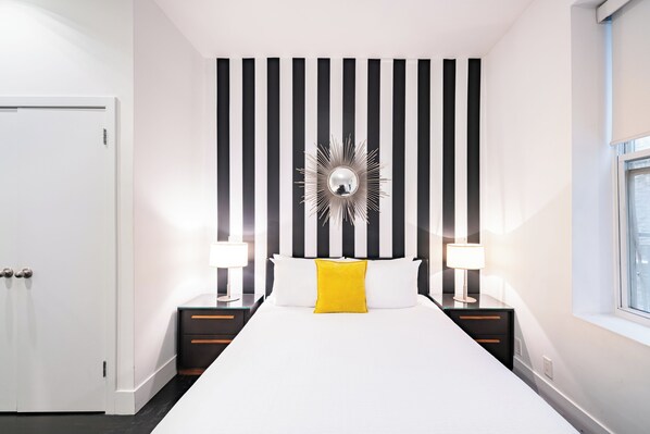 A hotel room with a large bed, two bedside tables with lamps, a black and white striped wall, and a window.