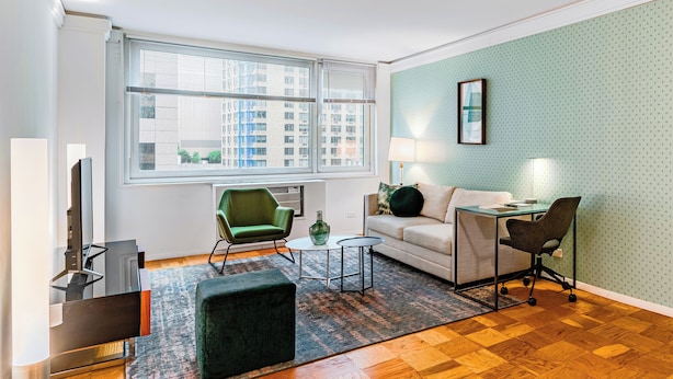 Un salon moderne avec un canapé, un fauteuil vert, une petite table, un téléviseur et une lampe.