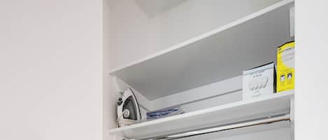 Un espacio pequeño para la lavandería con lavadora, plancha y escoba.