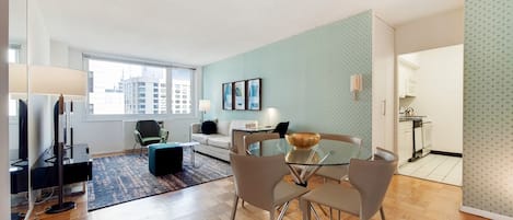 A modern living room with a glass dining table, a sofa, and a TV.
