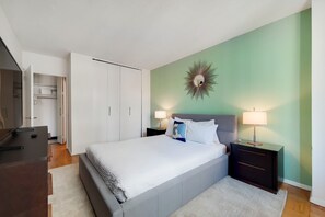 Un dormitorio con cama, mesitas de noche, armario y espejo en la pared.
