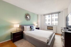 A bedroom with a bed, nightstands, a TV, and a window with blinds.