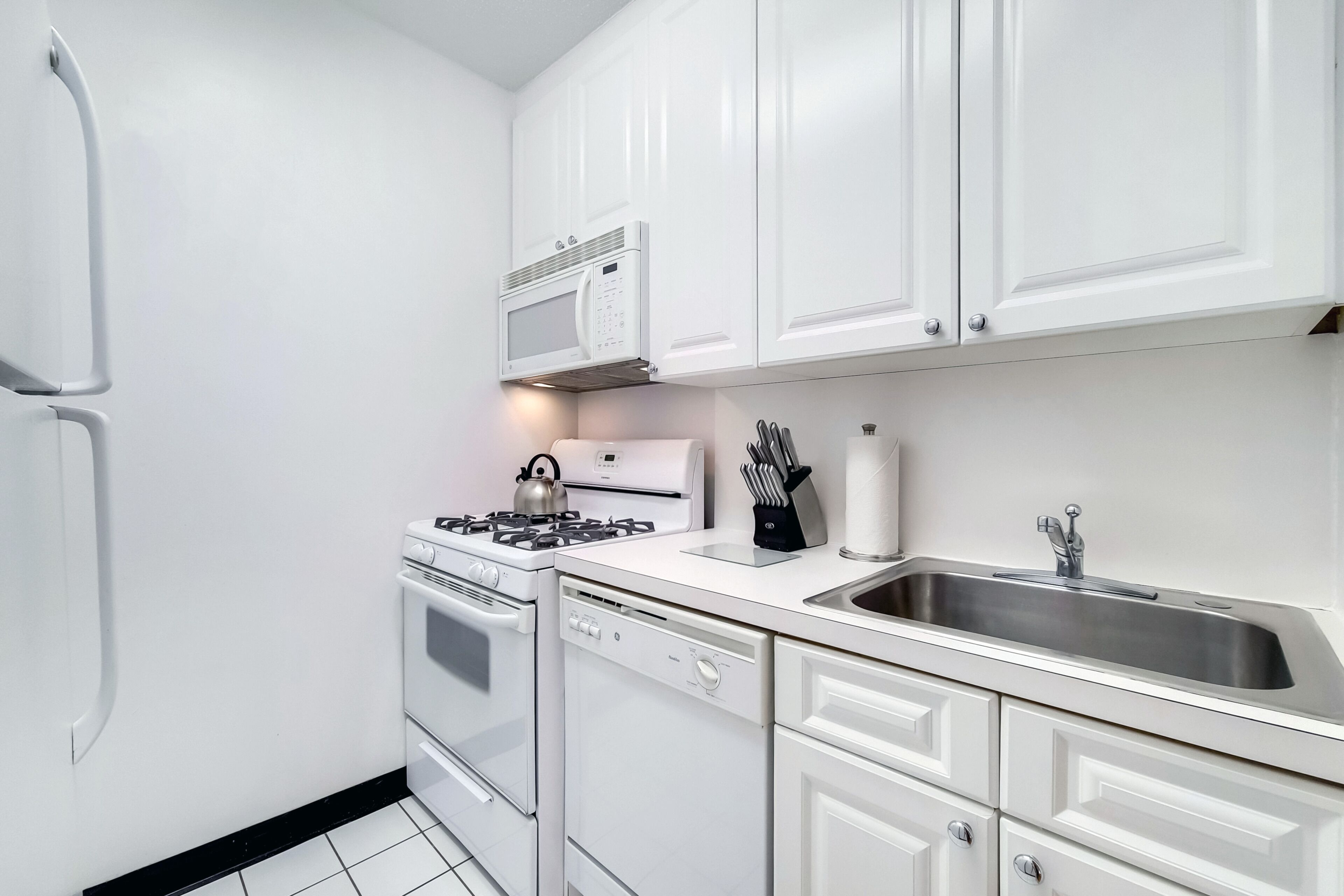 A modern kitchen with white cabinetry, a built-in microwave, a gas stove, a dishwasher, and a stainless steel sink.