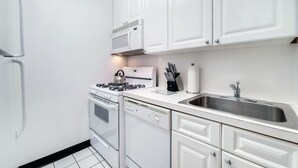 Une cuisine moderne avec des meubles blancs, un four à micro-ondes encastré, une cuisinière à gaz, un lave-vaisselle et un évier en acier inoxydable.
