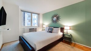 Une chambre à coucher avec un lit, deux lampes de chevet, une horloge murale et une fenêtre avec des stores.