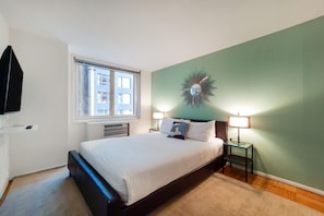Ein Schlafzimmer mit einem Bett, zwei Nachttischlampen, einer Wanduhr und einem Fenster mit Jalousien.