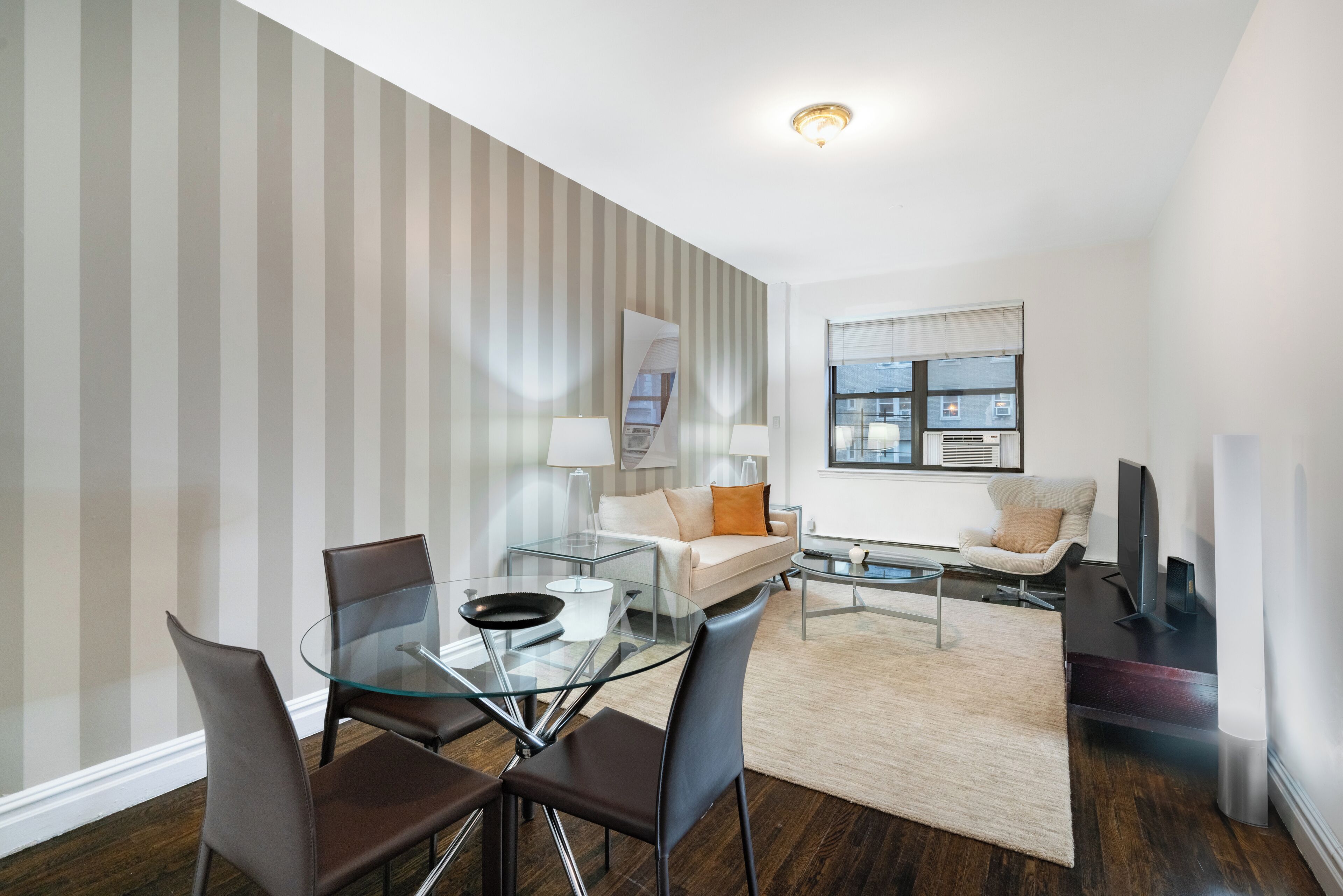 A modern living room with a glass dining table, leather chairs, a sofa, and a TV.