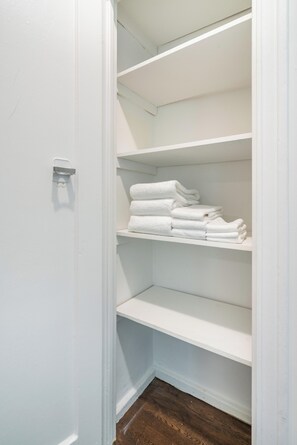 A white closet with shelves and a hanging rod, containing neatly folded white towels.